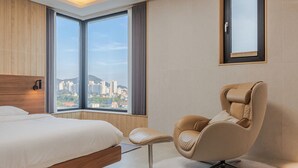 Hotellihuone, jossa on suuri ikkuna, sänky, tuoli ja seinällä oleva kehystetty kuva.