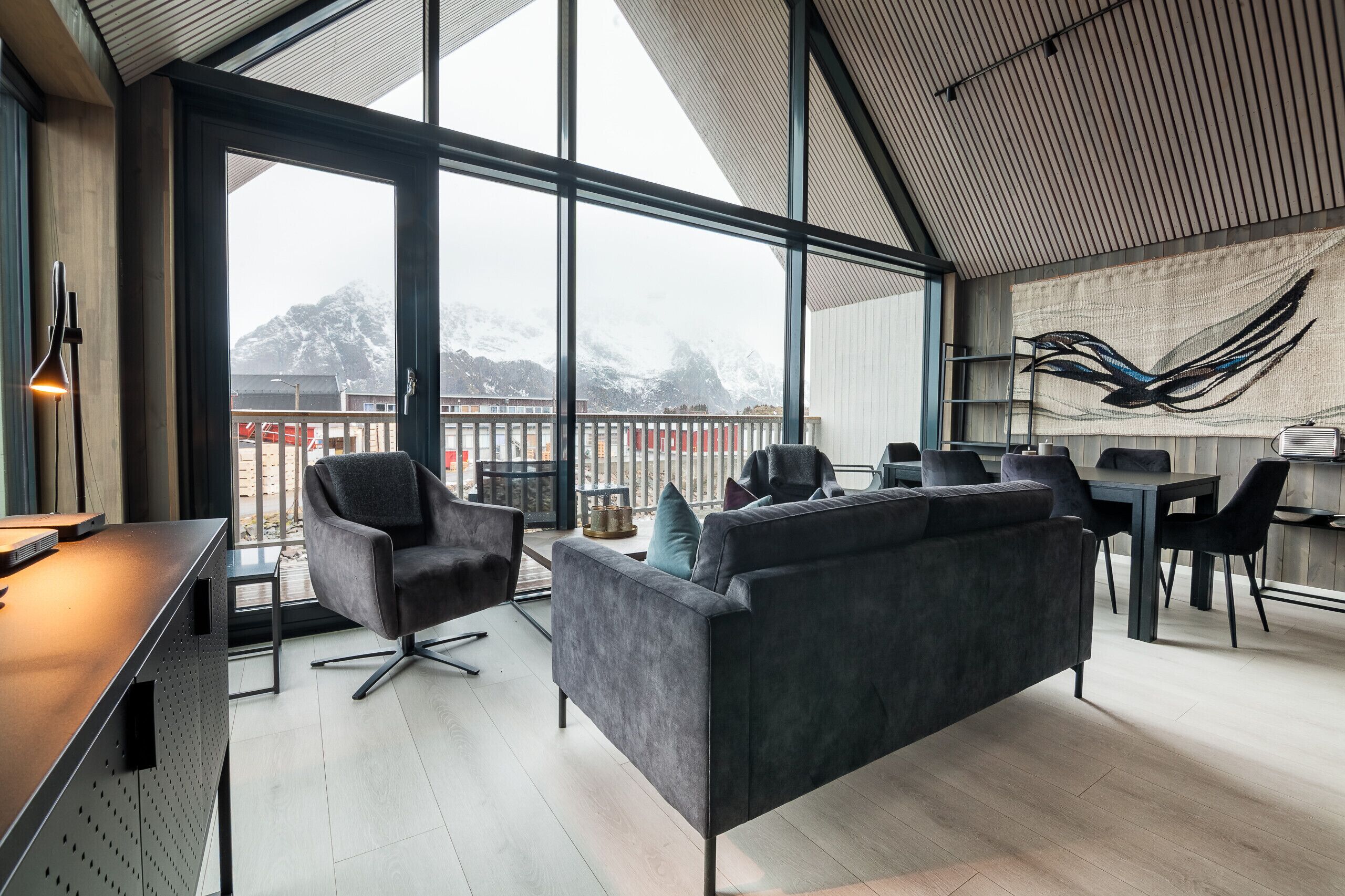 Ein modernes Interieur mit einer Couch, einem Esstisch, Stühlen, großen Fenstern mit Bergblick und einem Wandbild.