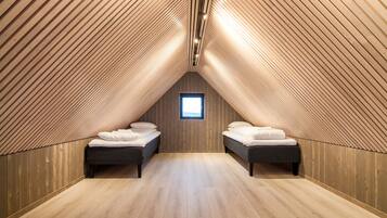 Une chambre mansardée avec des lambris en bois au plafond, deux lits, une petite fenêtre et un plancher en bois.