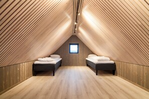 Une chambre mansardée avec des lambris en bois au plafond, deux lits, une petite fenêtre et un plancher en bois.