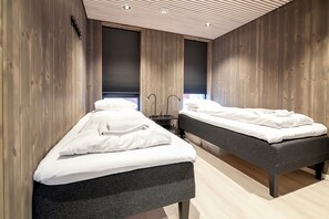 A modern room with two beds, wooden walls, and a ceiling with linear lighting.