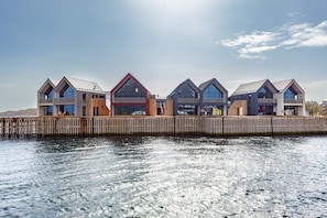 Ein Wohnhaus direkt am Wasser mit mehreren Wohneinheiten, Balkonen, großen Fenstern und einem hölzernen Steg.