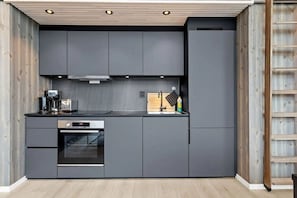 Eine moderne Küche mit grauen Schränken, einem eingebauten Backofen, einer Kaffeemaschine und einer Holzzieldecke.
