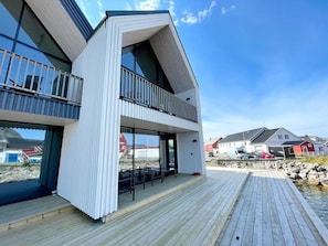 Un bâtiment moderne à deux étages, doté d’un balcon, de grandes fenêtres et d’une terrasse en bois.
