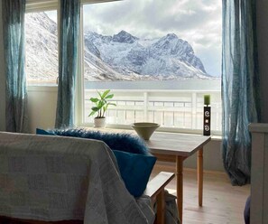 Una habitación con una cama, una mesa con un cuenco y una planta, y vistas a montañas nevadas a través de una ventana.
