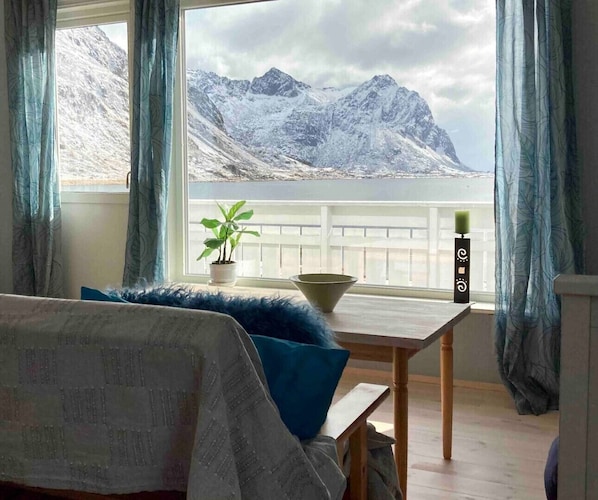 Une pièce avec un lit, une table sur laquelle se trouvent un bol et une plante, et une fenêtre donnant sur des montagnes enneigées.
