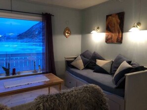 Un salon chaleureux avec un canapé, une table basse en bois et une vue sur un paysage montagneux par la fenêtre.