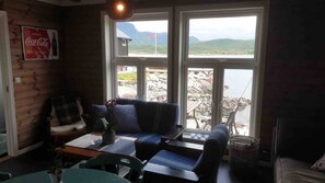 A cozy room with a sofa, a table, and a chair. There is a window with a view of a lake and mountains.