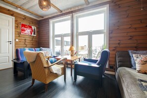A cozy room with a sofa, armchair, and a small table with a lamp. There are large windows and a door. - Arctic Lofoten Retreat - Enjoy the silence! (Vestvågøy)