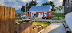 A red house with a white door, a wooden deck, and a garden with colorful flowers. - Arctic Lofoten Retreat - Enjoy the silence! (Vestvågøy)