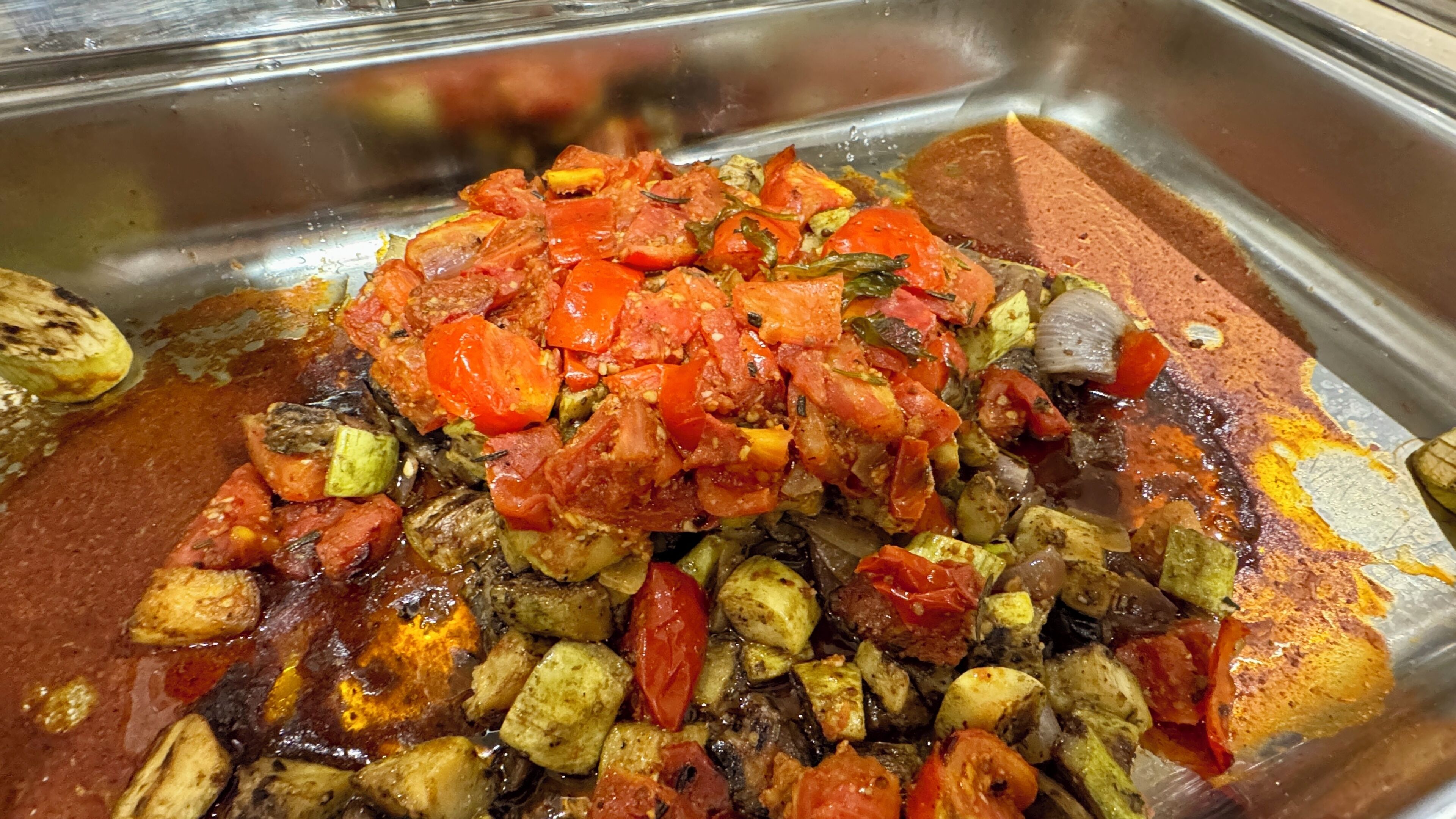 A buffet spread with a variety of cooked vegetables and a sauce.