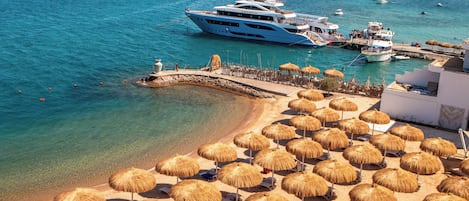 A coastal area with a beach, thatched umbrellas, and boats in the water.