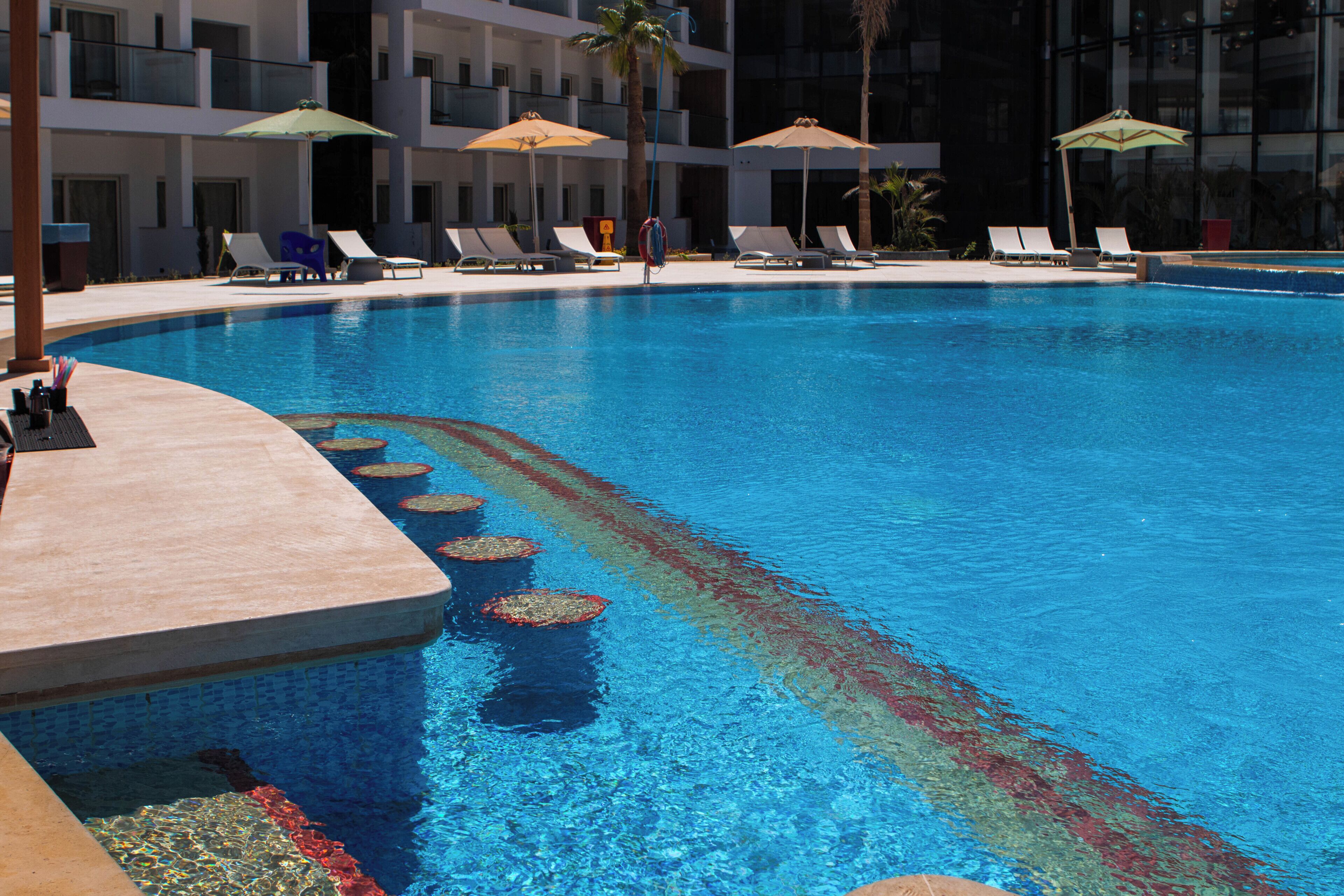 Una piscina con lettini e ombrelloni, circondata da un edificio con balconi.