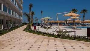 Zona de piscina en un resort con tumbonas, sombrillas y vista despejada al océano.