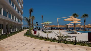 Zona de piscina en un resort con tumbonas, sombrillas y vista despejada al océano.