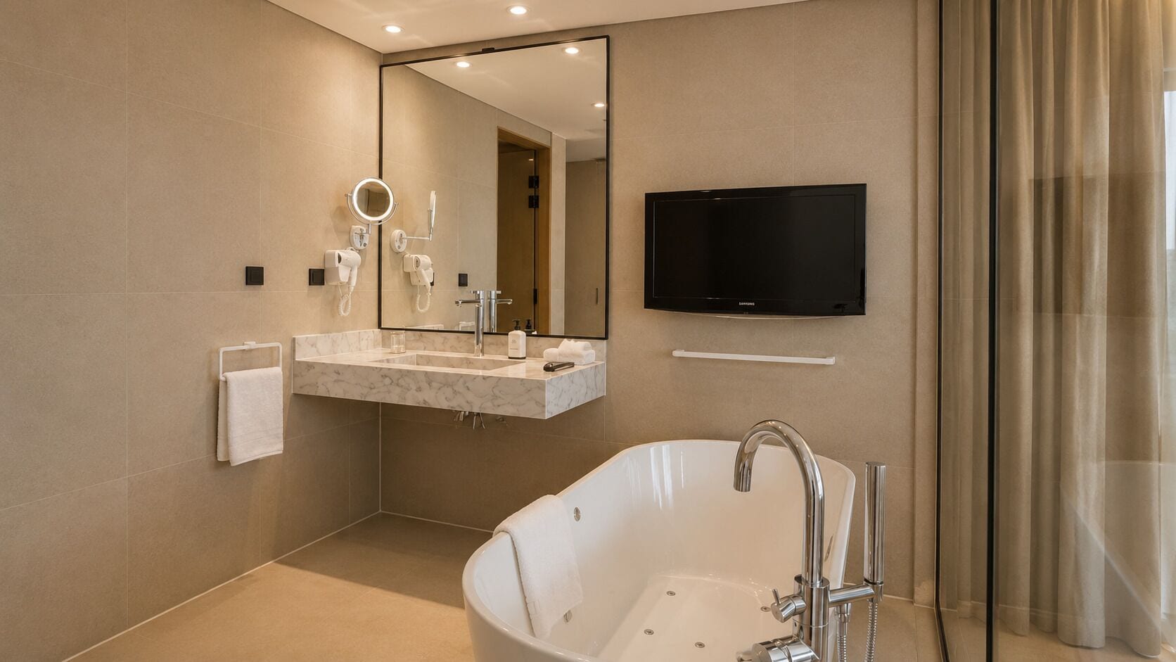 Une salle de bain moderne avec une baignoire sur pieds, un meuble-lavabo avec miroir et un téléviseur à écran plat fixé au mur.