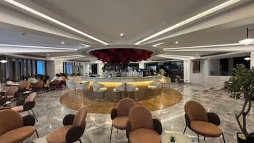 Una hall d'hotel moderna con un'area bar centrale, posti a sedere e un elemento decorativo a soffitto.
