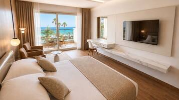 Habitación de hotel con una cama grande, un escritorio, un televisor y un balcón con vista al océano.