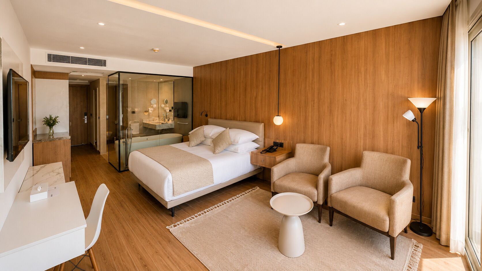 Una habitación de hotel moderna con cama, dos sillones, escritorio y mesita de noche.