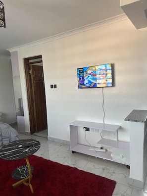 Ein Wohnzimmer mit Wand-Fernseher, einer weißen Unterhaltungsecke, einem roten Teppich und einem Marmorboden.