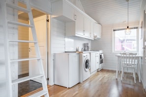 Une cuisine avec des meubles blancs, un lave-linge, un four et un coin repas comprenant une table et des chaises.