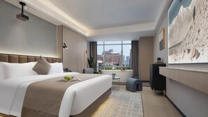 A modern hotel room with a large bed, a desk, a view of the city, and a painting on the wall.