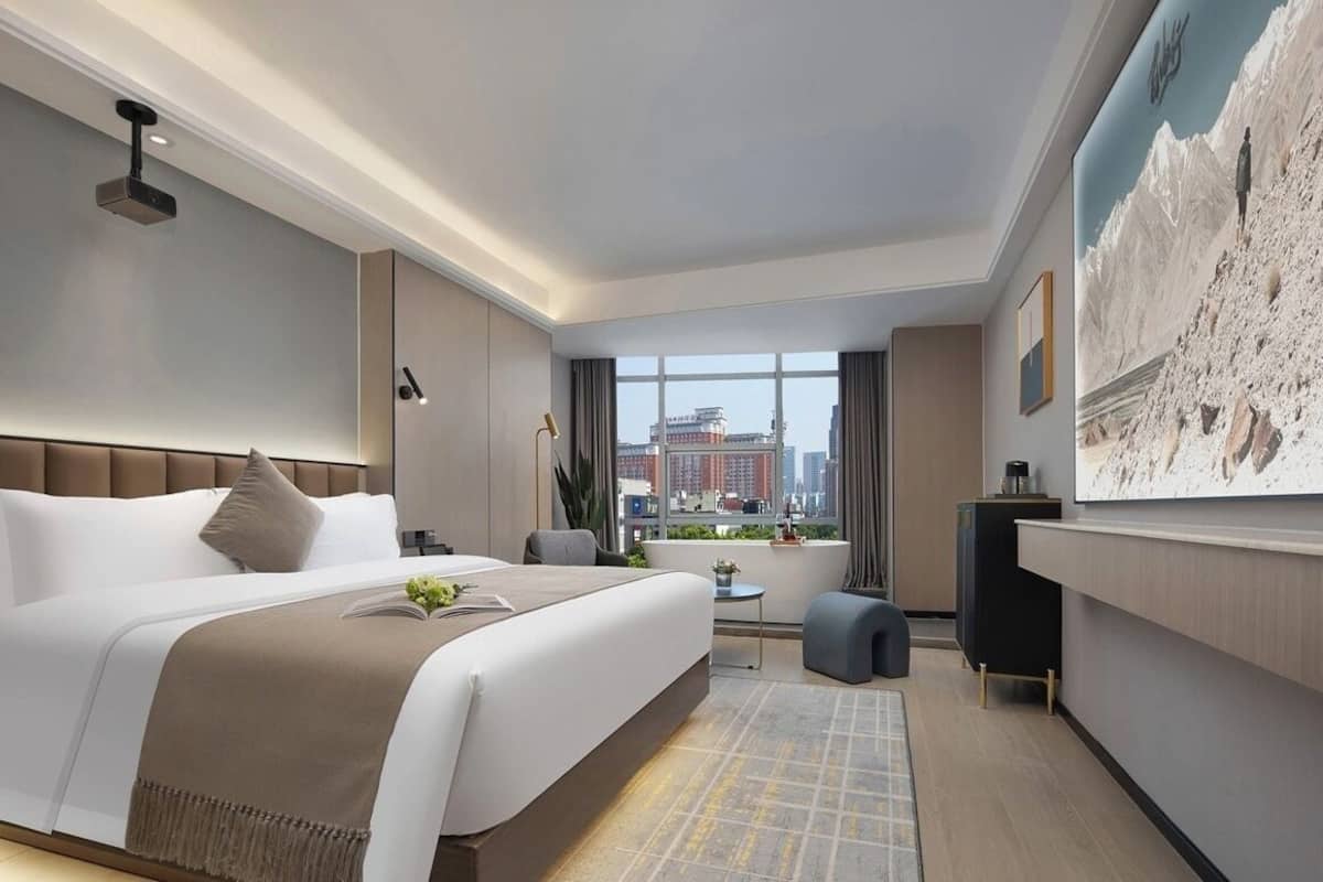 Una habitación de hotel moderna con una cama grande, un escritorio, vistas de la ciudad y un cuadro en la pared.