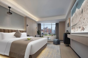 Habitació d'hotel moderna amb un llit gran, una taula de treball, vista a la ciutat i un quadre a la paret.