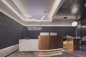 A hotel reception area with a marble counter, a wooden reception desk, and a modern ceiling design.