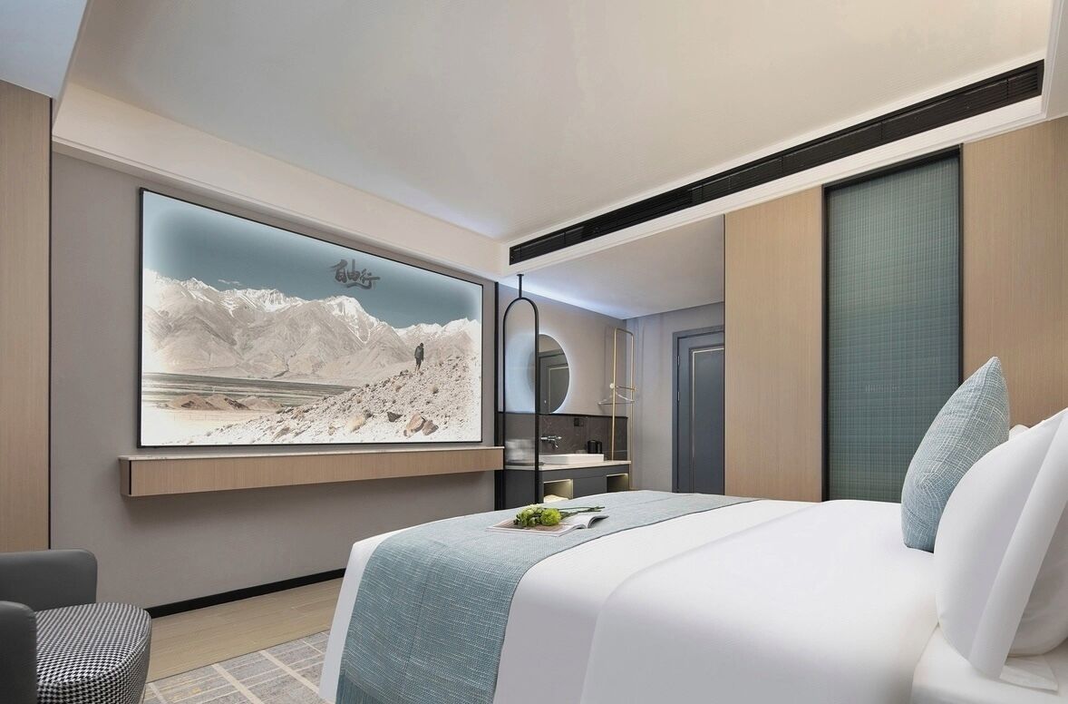 Ein modernes Hotelzimmer mit einem großen Bett, einem wandmontierten Fernseher, einem Schreibtisch und Bergblick.