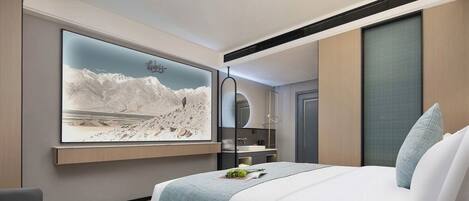 Ein modernes Hotelzimmer mit einem großen Bett, einem wandmontierten Fernseher, einem Schreibtisch und Bergblick.