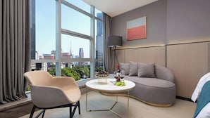A modern hotel room with a large window, a round table, a sofa, and a lamp.