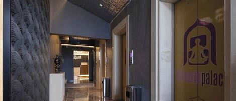 A modern hotel lobby with a patterned wall, a reception desk, and a door with the hotel name.