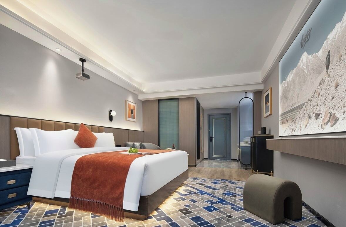 A modern hotel room with a large bed, a desk, a television, and a painting on the wall.