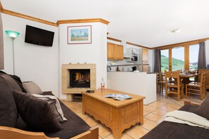 Ein Wohnzimmer mit Kamin, einem an der Wand befestigten Fernseher und einem Essbereich mit Holzmöbeln.