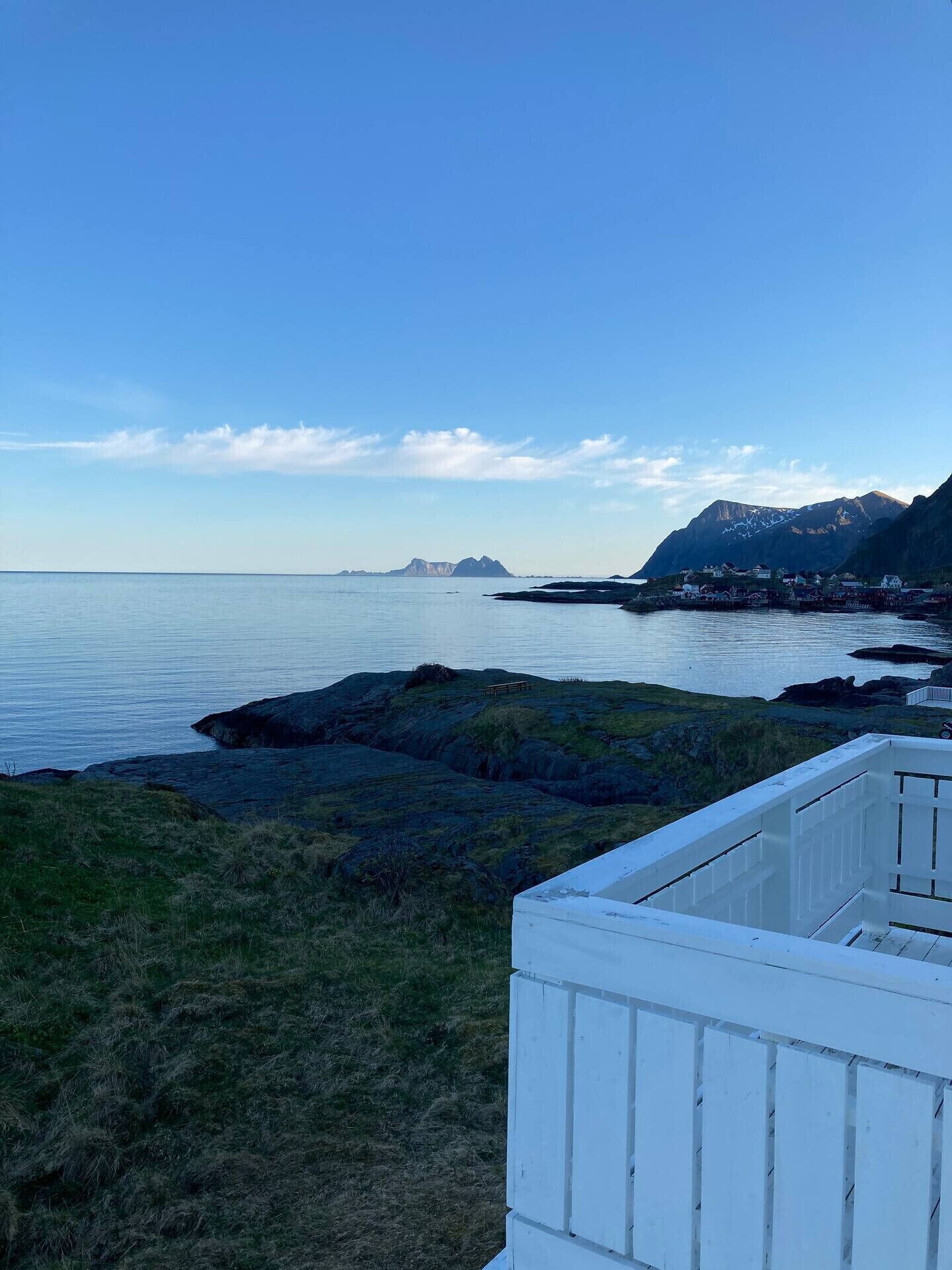 A coastal landscape with a clear sky, a body of water, and a small settlement with buildings near the shore.