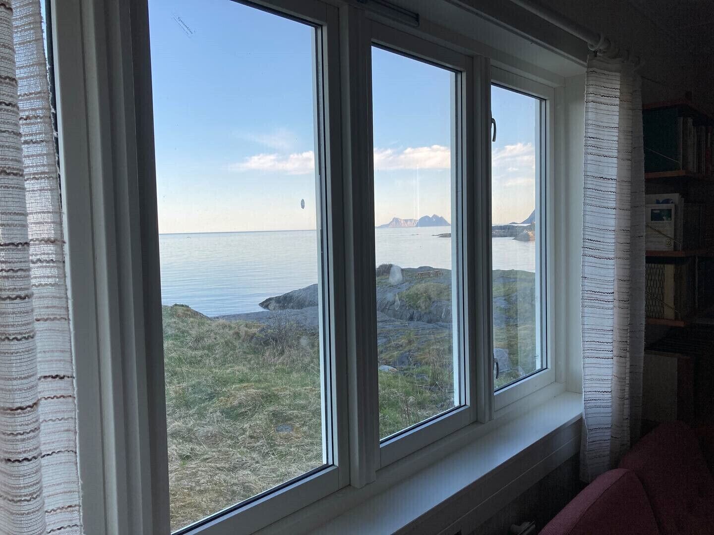 A room with a large window overlooking a coastal landscape, a bookshelf, and a red chair.