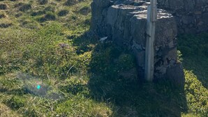 Een wit huis met een stenen muur en een houten paal in een grasveld, met bergen op de achtergrond.