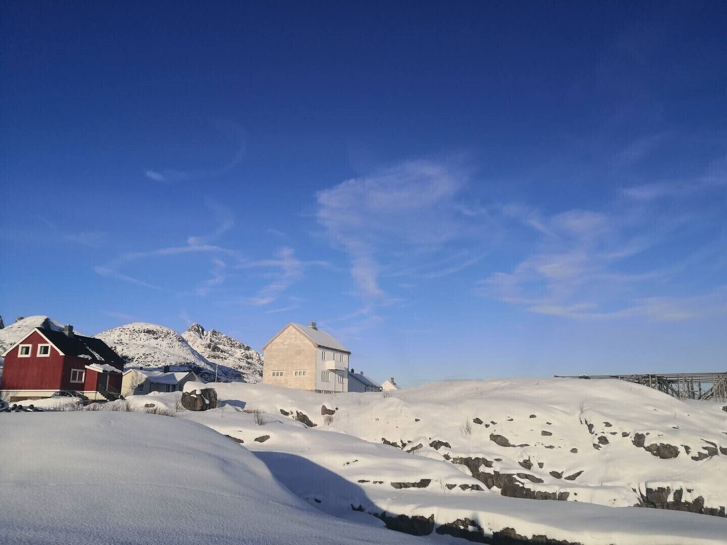 A snowy landscape with two buildings, one red and one beige, and a clear blue sky.