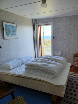 Een slaapkamer met een bed, een schilderij, een stoel en uitzicht op zee door een deur.