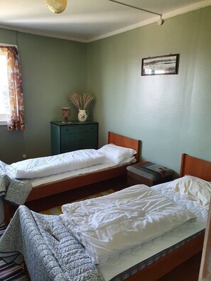 A room with two beds, a small table, a cabinet, and a framed picture on the wall.