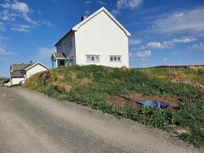 A white building with a gabled roof, a dirt road in front, and a grassy embankment.