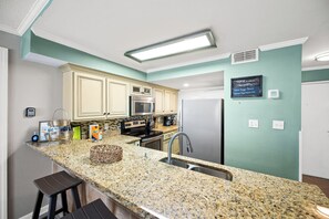 Una cocina con encimeras de granito, electrodomésticos de acero inoxidable y paredes color turquesa.