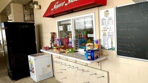 A snack shack with a red awning, a refrigerator, and a chalkboard menu.