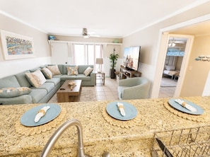 A living room with a sofa, a coffee table, a TV, and a kitchen area with granite countertops and a sink.