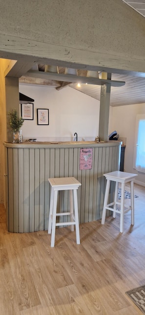 Een keuken met een houten kookeiland, twee witte barkrukken, een hanglamp en lijstjes met foto's aan de muur.