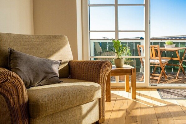 Ein Zimmer mit einer Couch, einem kleinen Tisch mit Stühlen, einer Topfpflanze und Blick durch ein großes Fenster.