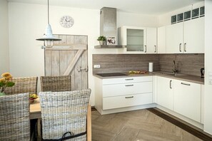 Eine moderne Küche mit weißen Schränken, einer Holztür und einem Essbereich mit Korbstühlen.