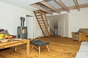Ein großzügiger Wohnbereich mit Holzboden, einer Couch, einem Tisch mit Früchten, einem Kamin und einer Treppe.