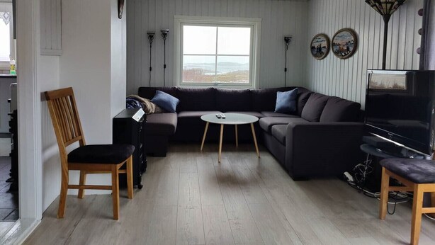 Ett vardagsrum med en hörnsoffa, ett runt soffbord, en tv och ett stort fönster.